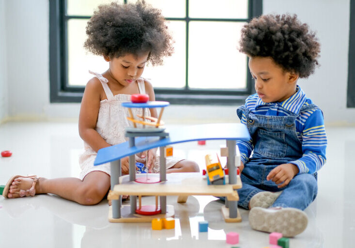 Two African brother and sister play some toys together in the room with day light with main focus on little girl.